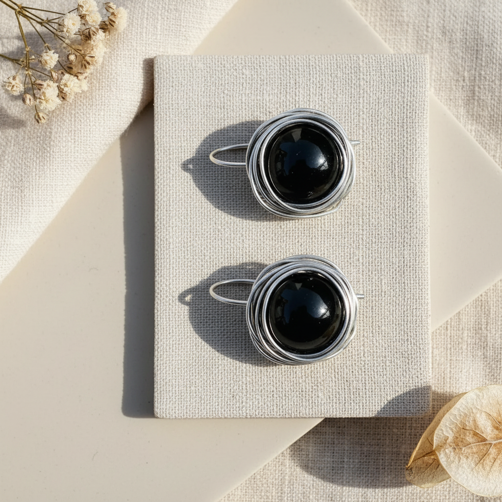Flat lay náušnice s obsidiánom v striebornom drôtovanom hniezde na ľanovej látke – Harakka Jewls