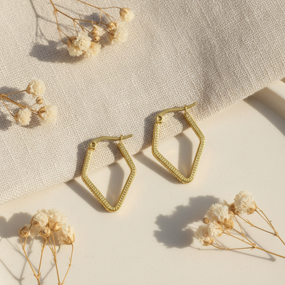 Zlaté geometrické náušnice s pleteným vzorom – luxusný flat lay Harakka